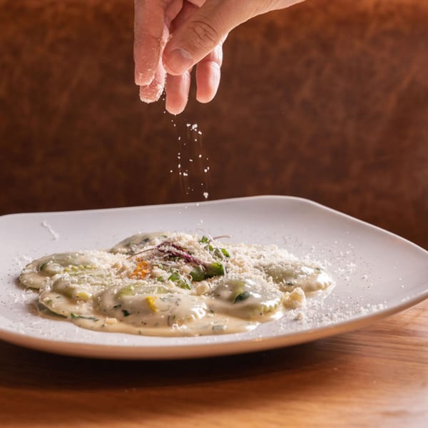 A hand sprinkles Parmesan cheese over Nardò Italian Restaurant's ravioli in a creamy sauce.