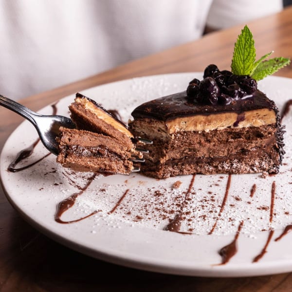 A fork lifts a piece of rich chocolate cake with berries and mint from a white plate.