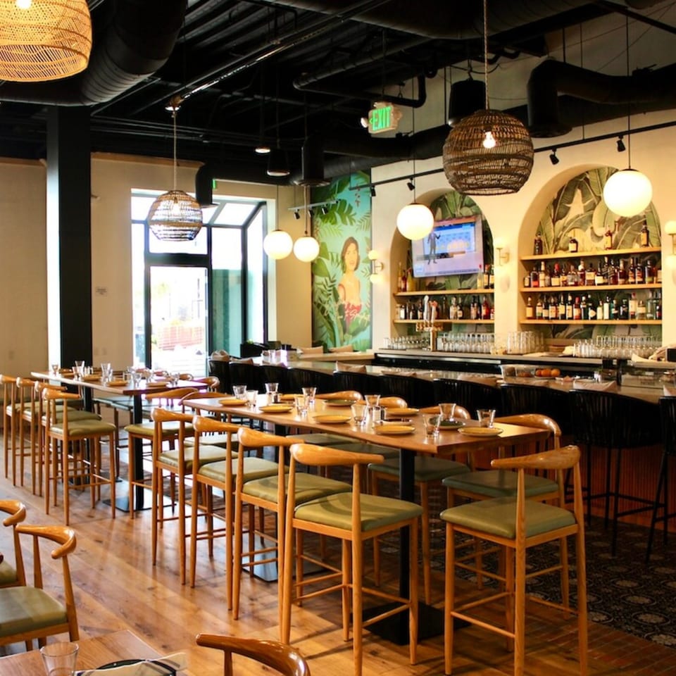 Nardò Italian Restaurant's dining room with high-top tables, chairs, and a bar with bottles and glasses.