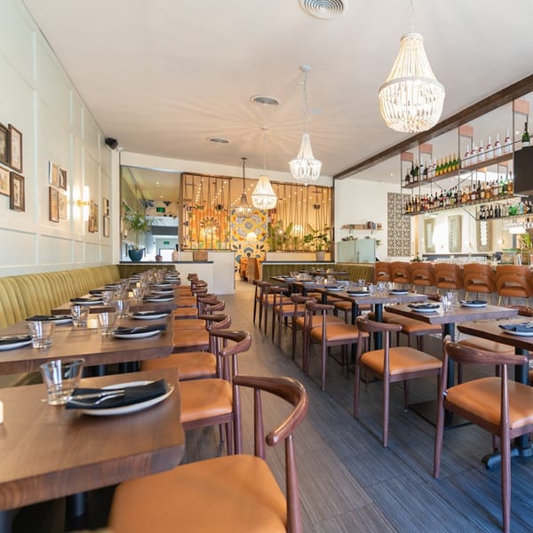 Nardò Italian Restaurant's dining room with set tables, olive green banquettes, and a full bar.