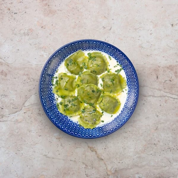 Nardò Italian Restaurant's green ravioli in a creamy sauce, garnished with herbs on a blue plate.