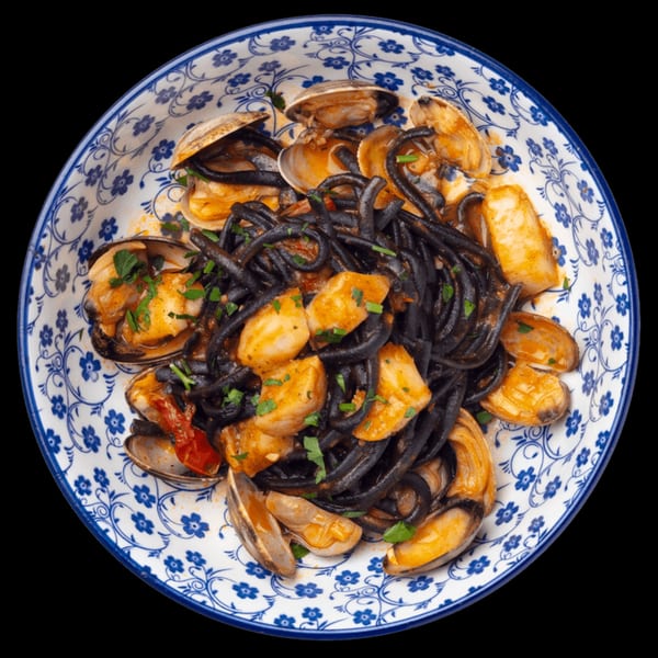 Black squid ink pasta with clams, mussels, and scallops in a white and blue patterned bowl.