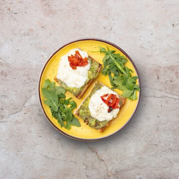 Two avocado toasts with burrata, roasted red peppers, and arugula on a yellow plate.