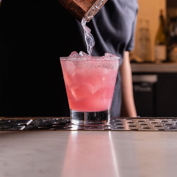 Bartender pouring a pink cocktail with ice into a sugar-rimmed glass at Nardò Italian Restaurant.