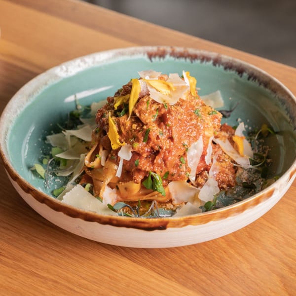 Nardò Italian Restaurant's pasta dish with red sauce, parmesan, and edible flowers in a blue bowl.