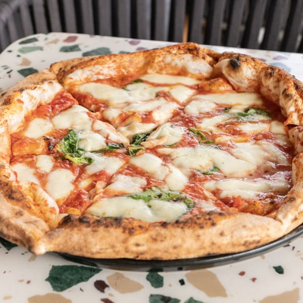 Nardò Italian Restaurant's Margherita pizza, with melted mozzarella, tomato sauce, and basil on a speckled table.
