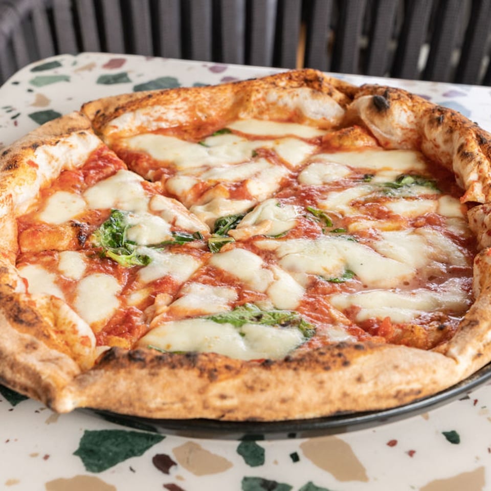 Nardò Italian Restaurant's Margherita pizza, with melted mozzarella, tomato sauce, and basil on a speckled table.