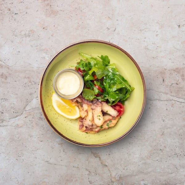 Fried calamari with a side of arugula salad, lemon wedge, and dipping sauce on a green plate.