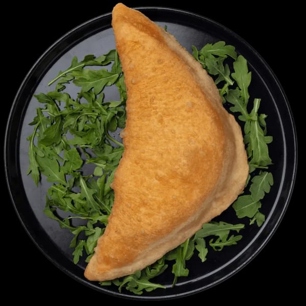 Golden-brown fried panzerotto on a black plate, surrounded by fresh green arugula leaves.