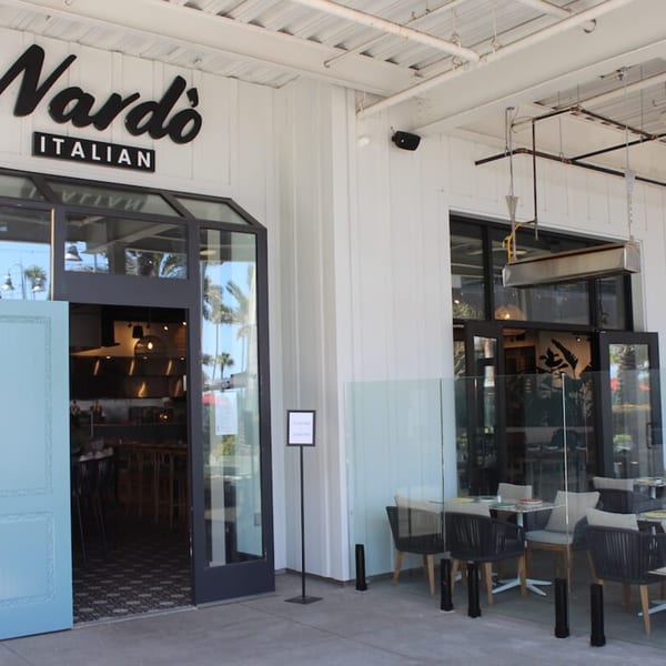 Exterior of Nardò Italian Restaurant with a light blue door, outdoor seating, and a white facade.