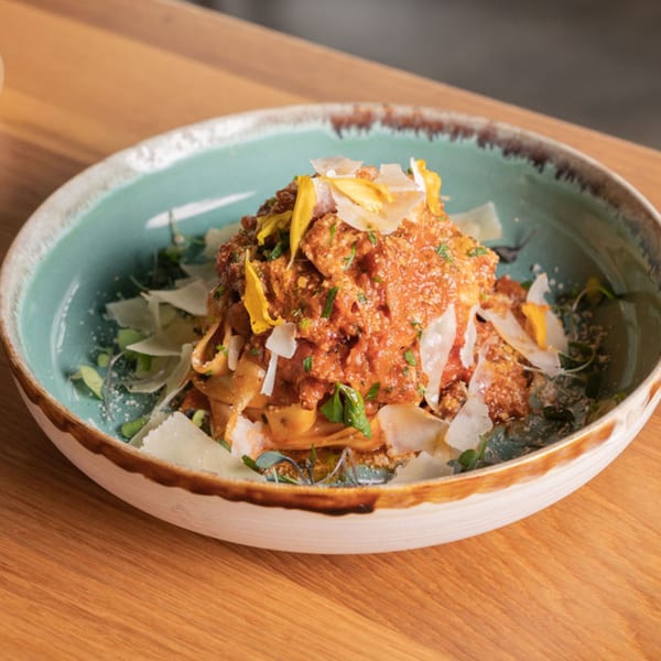 Nardò Italian Restaurant's pasta dish with red sauce, parmesan, and yellow edible flowers in a blue bowl.