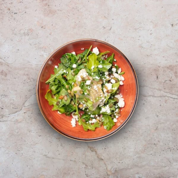 Nardò Italian Restaurant's fresh green salad with feta, pumpkin seeds, and artichoke hearts in an orange bowl.