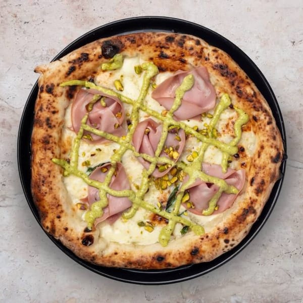Nardò Italian Restaurant's pizza with mortadella, pistachios, and a green sauce drizzle on a black plate.