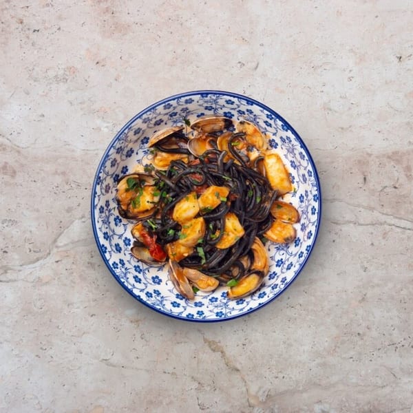 Nardò Italian Restaurant's squid ink pasta with clams and calamari in a blue and white patterned bowl.