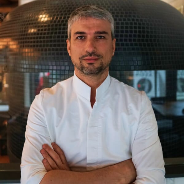 Nardò Italian Restaurant chef with gray hair and beard, wearing a white chef's coat, arms crossed.