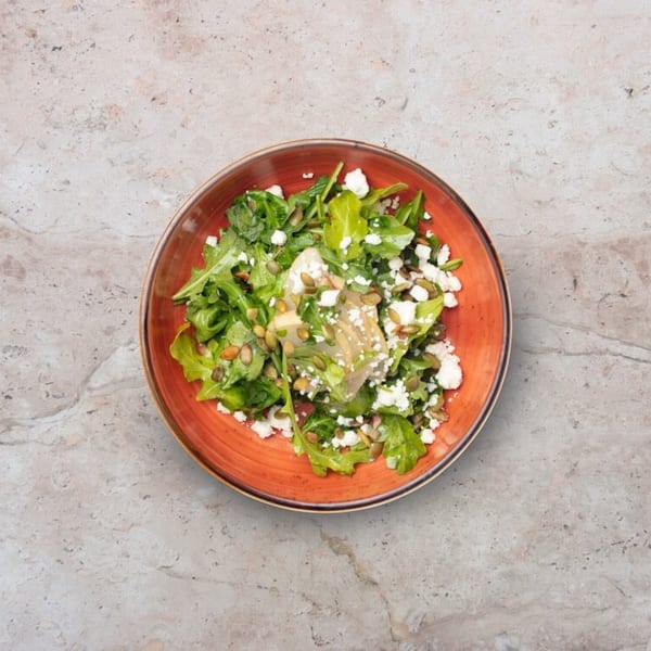 A vibrant Nardò Italian Restaurant salad with arugula, feta, pumpkin seeds, and artichoke hearts in an orange bowl.