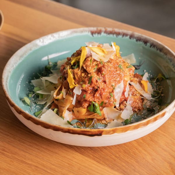 Nardò Italian Restaurant's pasta dish with red sauce, parmesan, and yellow edible flowers in a blue bowl.